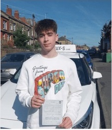 Ethan smiling holding his driving test pass certificate next to the SUX-S tuition car at Thornbury driving test centre in Bradford BD3
